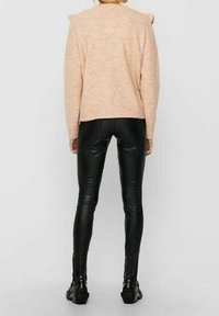 Różowy, nakrapiany sweter z detalami na ramionach, zestawiony z czarnymi, dopasowanymi skórzanymi spodniami i czarnymi botkami. Widok od tyłu na neutralnym tle.