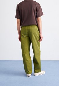 Gröna bomullsbukser med avslappnad passform, med bakfickor, tillsammans med en brun kortärmad t-shirt och vita sneakers.