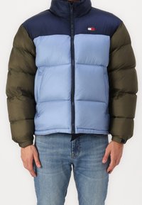 Prošívaná bunda s designem v barevných blocích v námořnické modři, světle modré a olivově zelené. Přední zip a vysoký límec. Měkká, prošívaná textura.