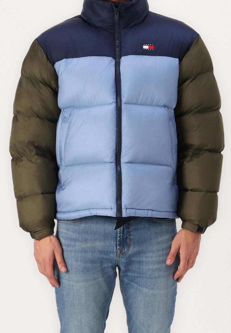 Prošívaná bunda s designem v barevných blocích v námořnické modři, světle modré a olivově zelené. Přední zip a vysoký límec. Měkká, prošívaná textura.