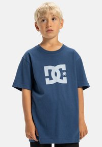 Blaues Baumwoll-T-Shirt mit einem großen weißen DC-Logo und Stern-Graphic auf der Vorderseite. Kurze Ärmel und runder Ausschnitt.