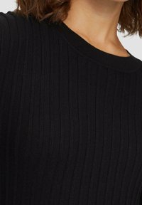 Pull noir côtelé avec un col rond, présentant des lignes verticales texturées et un tissu tricoté doux. Des accents incluent une couleur noire classique.