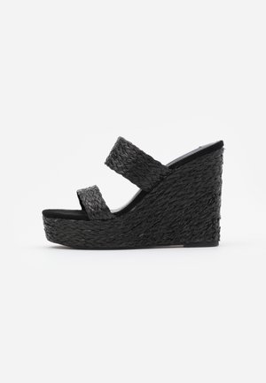 Schwarze Keilsandalen mit gewobener Textur, zwei breiten Riemen, offener Zehenpartie und einem auffälligen Wedge-Absatz. Schlichte und strukturierte Silhouette.