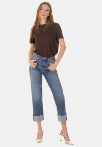 T-shirt marrone, jeans azzurri a vita alta con orli arrotolati e scarpe con tacco alto argentate e lucide. Design semplice e vestibilità casual.