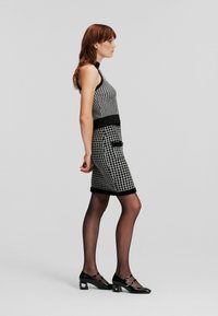 Rochie cu imprimeu alb și negru, cu o siluetă ajustată, design fără mâneci și un cordon negru în talie. Asortată cu pantofi cu toc negri și strălucitori.