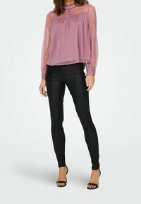 Blouse lavande ample et transparent avec un motif texturé, encolure ronde et détails de boutons, associée à un pantalon en cuir noir ajusté.