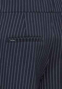 Tissu à rayures bleu marine avec une texture lisse ; présente une poche arrière unique et de fines rayures blanches pour un détail supplémentaire.