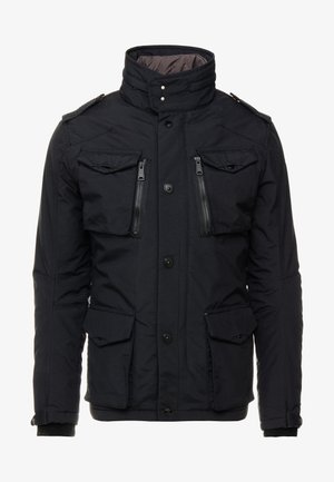 Zwarte jas met hoge kraag, ritssluitingen en flapzakken, drukknopen en knoopsluitingen, en geribbelde manchetten. Materiaal is glad met een lichte glans.