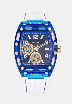 Montre carrée bleue avec bracelet blanc, accents dorés, deux sous-cadrans et chiffres blancs, nom de la marque "GUESS" sur le cadran.