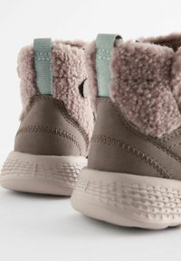 Braune Wildleder-Ankle-Boots mit einem weichen, rosafarbenen Plüschkragen, strukturierten Gummisohlen und hellblauen Ziehschlaufen für ein einfaches Anziehen.