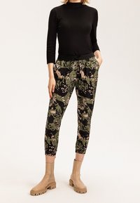 Top ajustado de manga larga negro; joggers verdes con patrón de camuflaje, con cinturilla elástica y bolsillos; llevados con botas de tobillo beige.