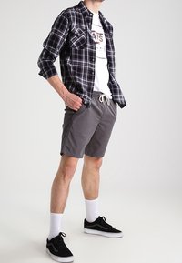 Koszula w kratę w czerni i szarości na białej koszulce z grafiką, zestawiona z szarymi szortami, białymi skarpetkami i czarnymi trampkami. Styl casual.