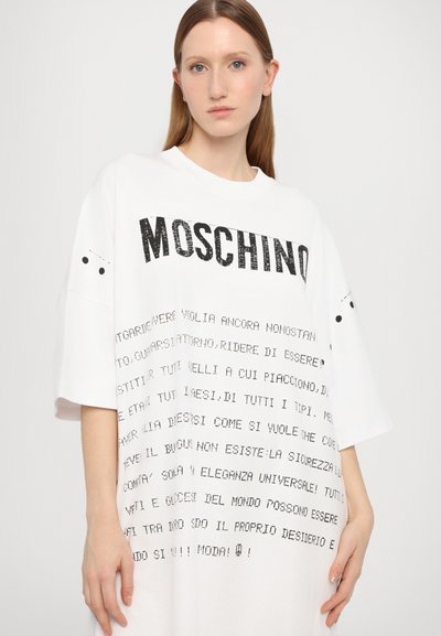 Túlméretezett feh�ér póló fekete felirattal. Kerek nyakkivágása és rövid ujjai vannak. A nyomaton szerepel a "Moschino" márkaneve és különféle szövegminták.