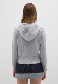 Maglione grigio con cappuccio, orlo e polsini a coste, caratterizzato da una texture morbida. Abbinato a una gonna di denim, che crea un aspetto stratificato.