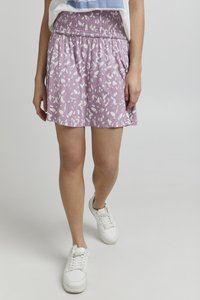 Lilla nederdel med et hvidt abstrakt mønster, der har en smocket talje. Parret med hvide sneakers, vist fra taljen og ned.