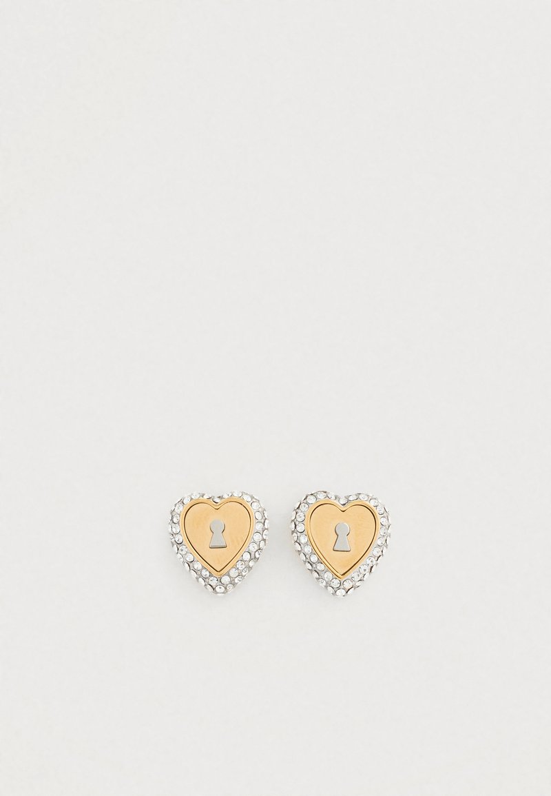 Ασημί καρφωτά σκουλαρίκια σε σχήμα καρδιάς με χρυσή τρύπα κλειδιού στο κέντρο, περιτριγυρισμένα από μικρές διαφανείς στρας για επιπλέον λεπτομέρεια.