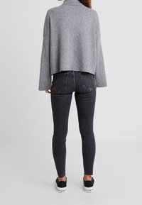 Grijze cropped trui met hoge kraag, gecombineerd met zwarte skinny jeans. Sneakers hebben witte zolen en een zwarte bovenkant.