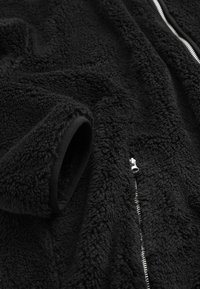Schwarz fleecejacke mit einer weichen, strukturierten Oberfläche. Mit Reißverschluss und elastischen Bündchen, die ein gemütliches und warmes Design betonen.