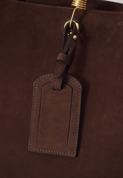 Geanta tote din suede maro, cu un tag din piele cu borduri cusute și un accent din metal auriu pentru închidere.