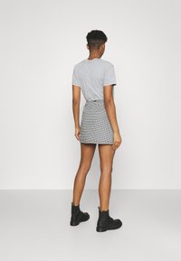 Grå t-shirt, kort ärm; svart och vit houndstooth minikjol; svarta ankelboots med snörning och kraftiga sulor; enfärgad bakgrund.