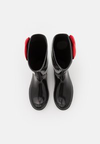 Svarta blanka gummistövlar med en slät yta och rundade tår. Röda accentfärger högst upp ökar synligheten. Klassisk knähög design.