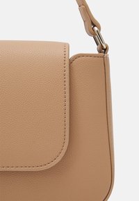 Beige läderhandväska med texturerad yta, rundad klappstängning och guldfärgade beslag. Har snygga sömmar och en kompakt design.