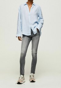 Camisa de botones a rayas azul claro con cuello, combinada con jeans gris ajustados y zapatillas de colores.