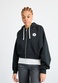Black cropped hoodie in cotton blend, featuring a front zipper, kangaroo pockets, and a stitched logo patch with a star. White drawstrings.