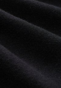 Primo piano di un morbido tessuto nero con texture a maglia visibile e pieghe delicate.