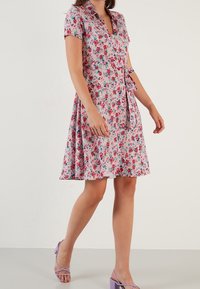 Květnaté šaty v růžové barvě s límečkem, krátkými rukávy a vypasovaným živůtkem. Mají pásek v pase a rozšířenou sukni s květinovým vzorem.