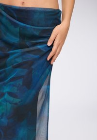 Niebieska przezroczysta spódnica w stylu wrap z abstrakcyjnym kwiatowym wzorem w różnych odcieniach niebieskiego i zielonego. Gładka tekstura z drapowanym krojem.