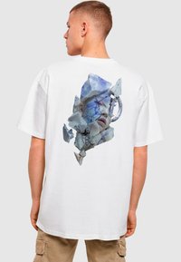 Weißes Baumwoll-T-Shirt mit einem blauen und grauen fragmentierten Gesichtsgrafik auf der Rückseite. Lockerer Schnitt mit kurzen Ärmeln.