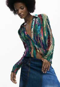 Cardigan texturé multicolore à manches longues, boutonné sur le devant avec un décolleté en V profond, associé à une jupe en jean foncé.
