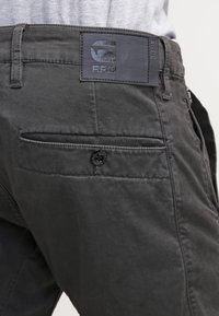 Svarta bomullbyxor med texturerad yta, utrustade med en logotypmärke på midjebandet, sidfickor och en knappdetalj på bakfickan.