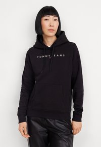Sudadera negra con cordones, bolsillo frontal y "TOMMY JEANS" impreso en blanco en el pecho. Fabricada con una suave tela texturizada.