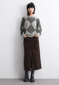 Grau und schwarz karierter Pullover mit lockerer Passform, kombiniert mit einem braunen Cordrock mit Schlitz vorne und schwarzen kniehohen Plateau-Stiefeln.