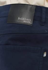 Pantalon bleu marine avec une étiquette en cuir portant la mention "Jack & Jones Since 1990", doté d'une poche latérale et d'une texture en coton lisse.
