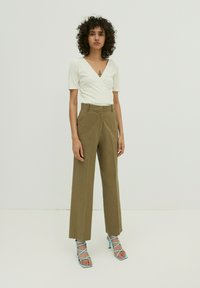 Witte mouwloze wikkeltop, khaki hoge taille wijde broek, blauwe strappy hakken. Effen textuur, minimalistisch ontwerp, kleding met een op maat gemaakte pasvorm.
