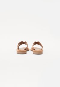 Braune Leder-Sandalen mit flacher Sohle, die über gewölbte Riemen und ein offenes Rückendesign verfügen und eine glatte Textur sowie eine schlichte Struktur aufweisen.