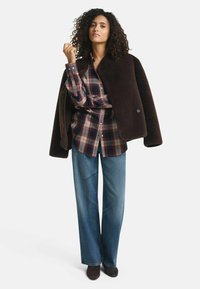Bruine bont-stijl oversized jas, rood en marineblauw geruit shirt, wijde denim jeans en donkerbruin enkellaarsjes.