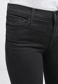 Black denim jeans with a fitted design, a small front pocket, and a smooth texture. Features a button closure and belt loops.