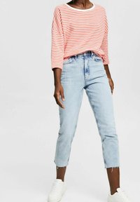 Pruhované červeno-bílé oversized triko s dlouhým rukávem, spárováno se světle modrými džínami rovného střihu, které mají roztrhaný lem, a bílými sneakers.