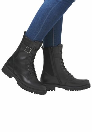 Bottines noires avec une combinaison de cuir lisse et de panneaux latéraux élastiques. Présente une boucle en métal, des lacets et une semelle robuste et texturée.