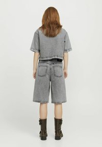 Top corto de mezclilla gris con bordes deshilachados, combinado con pantalones cortos de mezclilla gris. Textura duradera y bolsillos traseros prominentes. Lleva botas negras hasta la rodilla.