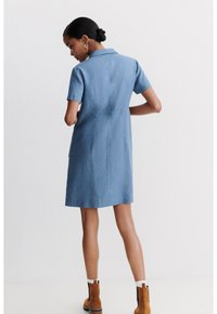 Vestito camicia in lino blu con maniche corte, colletto e taglio dritto; presenta tasche laterali e lunghezza sotto il ginocchio.