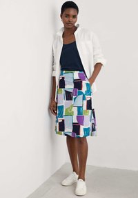 Falda de colores múltiples y con un diseño estampado que presenta formas abstractas en púrpura, verde, azul y negro, combinada con una blusa azul marino y zapatillas blancas.