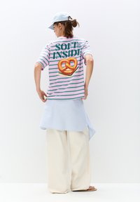 Gestreept roze en groene T-shirt met korte mouwen, voorzien van een pretzel-afbeelding en de tekst "SOFT ON THE INSIDE" op de achterkant; gecombineerd met een lichtblauwe rok.