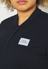 Námořnická modrá polo košile s texturovanou tkaninou, vybavená dvouknoflíkovou légou a čtvercovou nášivkou loga Tommy Hilfiger na hrudi.