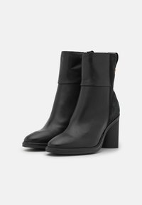 Bottines noires en cuir avec une finition lisse. Dotées d'un talon épais et d'une fermeture éclair sur le côté. Texture douce à l'arrière.