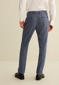 Férfi kék mintás nadrág, textúrált felülettel, oldalsó és hátsó zsebekkel, slim fit szabással, fekete bőrcipővel párosítva.